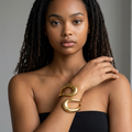 Model trägt den girlzhood Power Bracelet Eléa, einen geschwungenen, skulpturalen Armreif aus goldener Legierung.