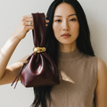 girlzhood Luxe Knot Clutch in Burgundy aus PU-Leder mit goldenem Verschluss, gehalten von einer Frau