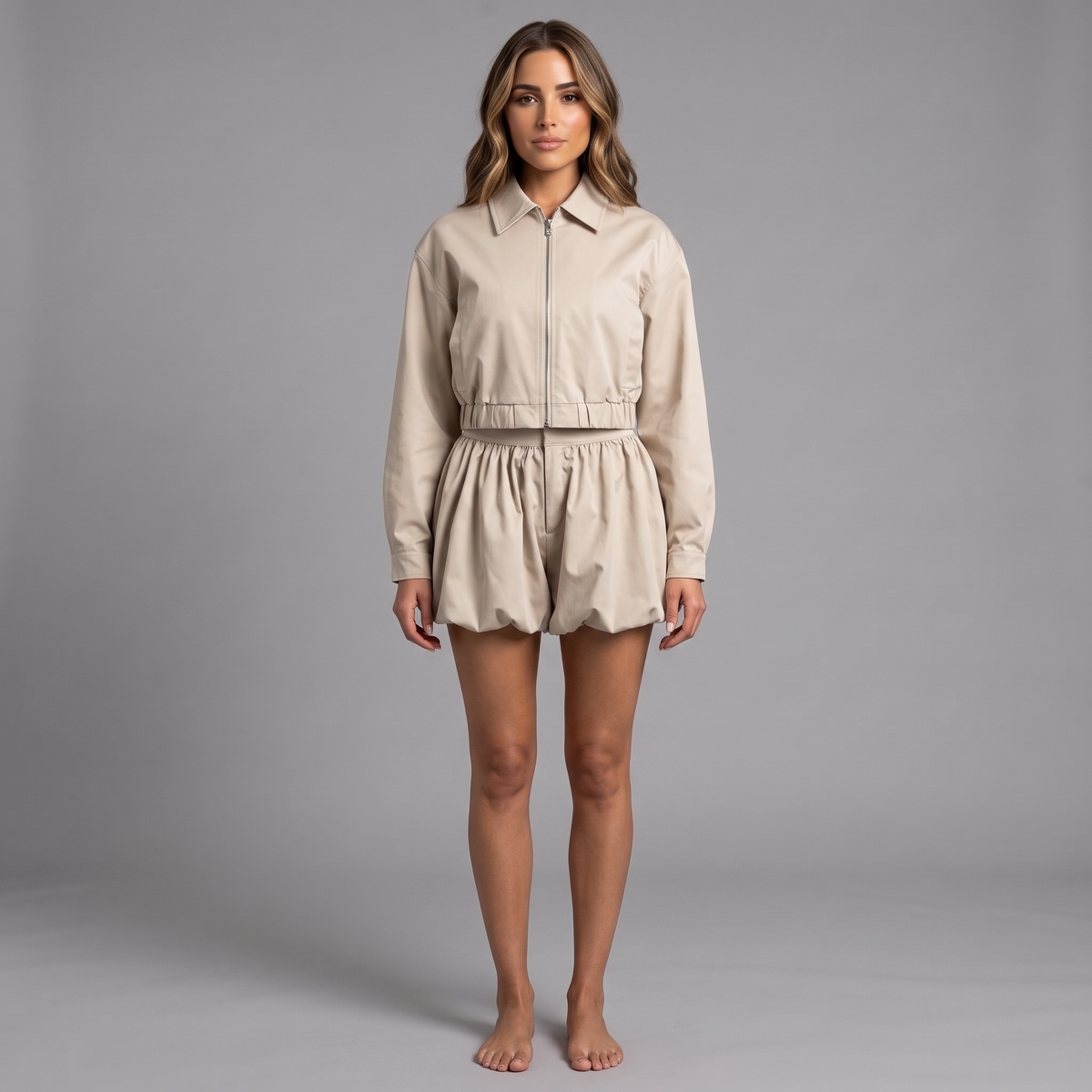 Model trägt das girlzhood Milano Cartel Set in Creme-Beige mit Cropped Jacke und Balloon Shorts vor grauem Hintergrund