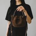 girlzhood Sienna Suede Handtasche in Dunkelbraun mit Knoten-Details und Veloursleder-Optik in der Hand gehalten