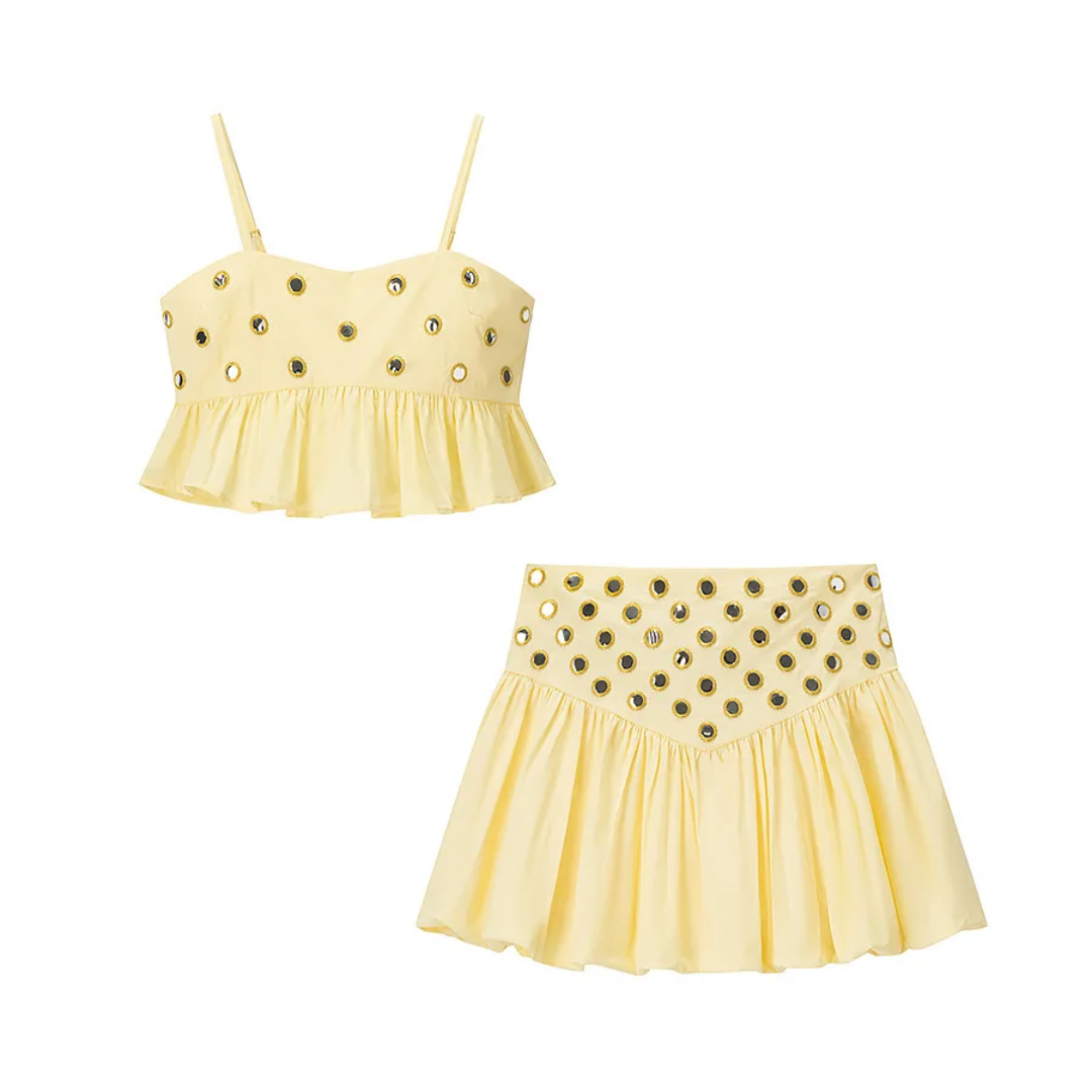 girlzhood Vespera Luxe Set in Soft Lemon mit Rüschentop und ausgestelltem Rock, verziert mit goldenen Glanz-Akzenten.